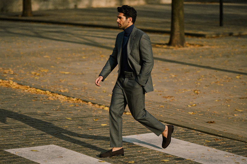 A man in a mid-grey suit with a navy roll-neck crossing a city square on an autumn morning